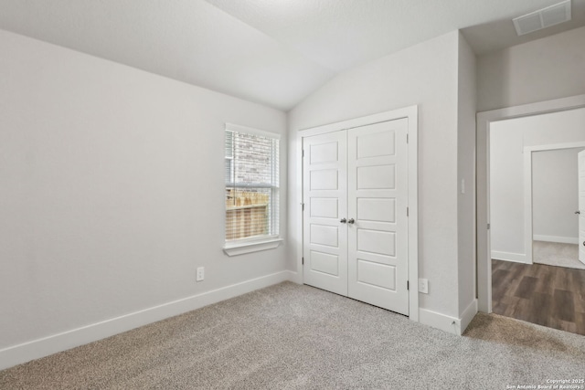 unfurnished bedroom featuring vaulted ceiling, a closet, and carpet flooring