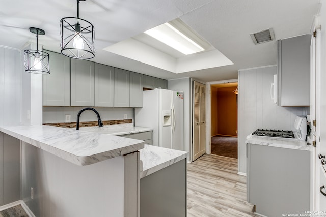 kitchen featuring white appliances, gray cabinetry, kitchen peninsula, hanging light fixtures, and light hardwood / wood-style floors