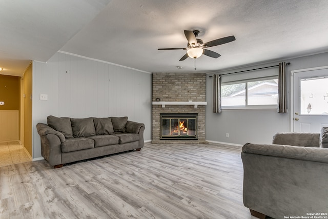 living room featuring a fireplace, a textured ceiling, ceiling fan, crown molding, and light hardwood / wood-style flooring