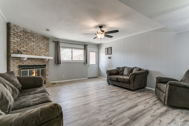 living room featuring light hardwood / wood-style flooring, wood walls, ceiling fan, and a brick fireplace