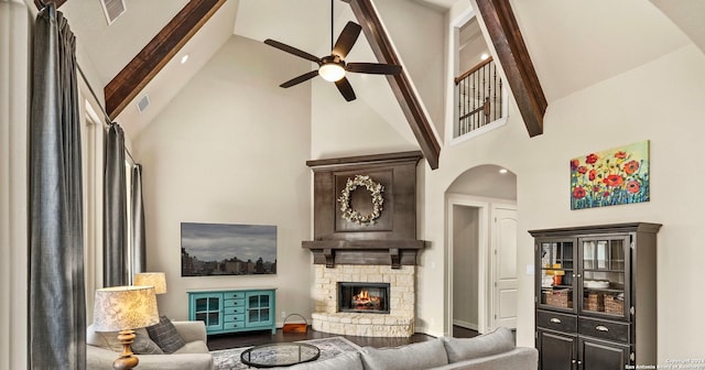 living room with wood-type flooring, a stone fireplace, ceiling fan, beam ceiling, and high vaulted ceiling