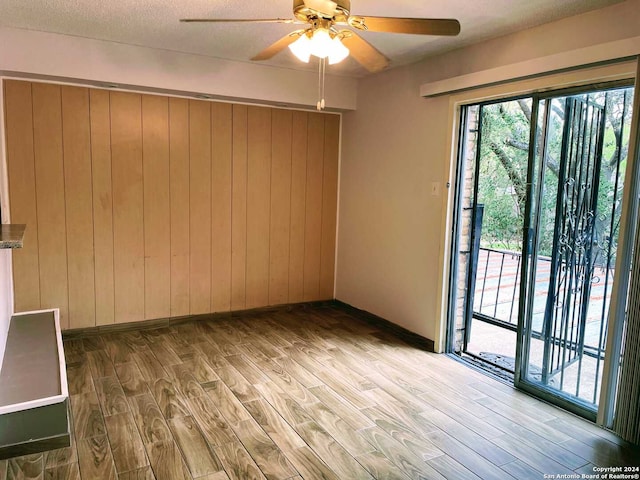 unfurnished room with ceiling fan, wood walls, a textured ceiling, and light hardwood / wood-style flooring