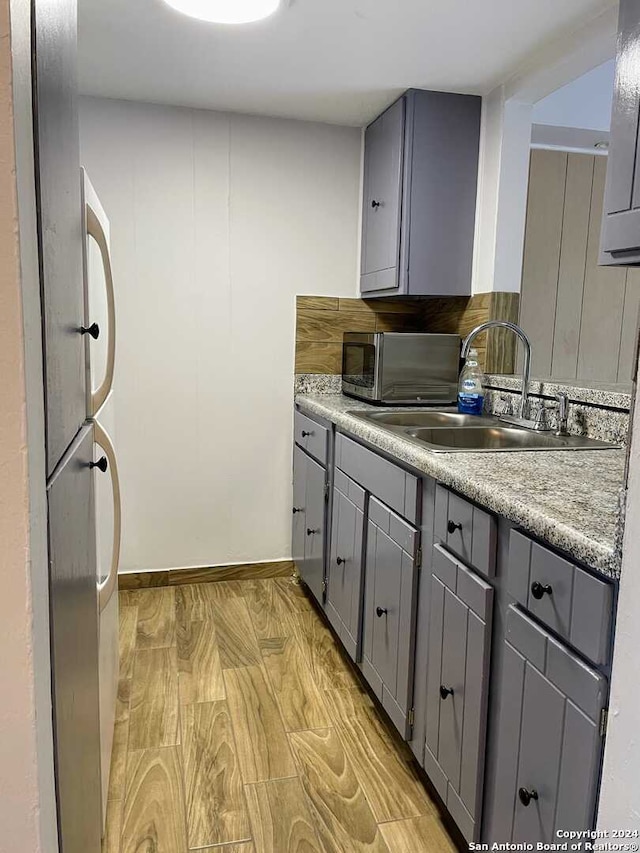 kitchen with appliances with stainless steel finishes, light hardwood / wood-style flooring, sink, and gray cabinetry