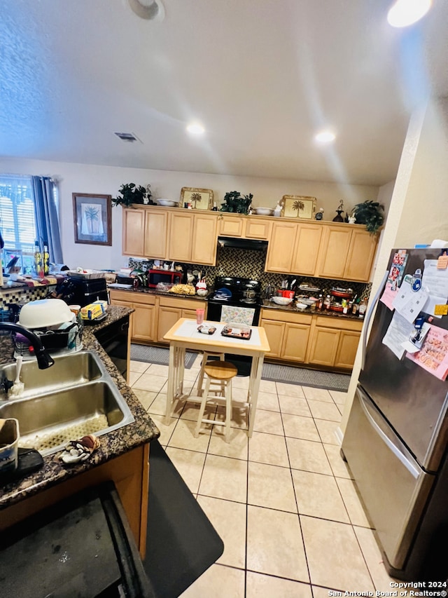 kitchen with light brown cabinets, sink, dark stone counters, and stainless steel refrigerator