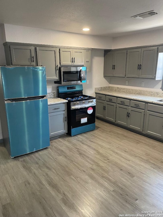 kitchen with gray cabinetry, stainless steel appliances, and light hardwood / wood-style flooring