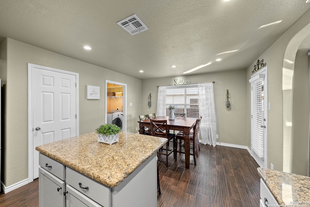 kitchen featuring separate washer and dryer, a textured ceiling, a center island, light stone counters, and dark hardwood / wood-style floors