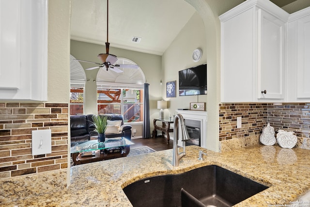 kitchen featuring sink, backsplash, vaulted ceiling, light stone counters, and hardwood / wood-style flooring