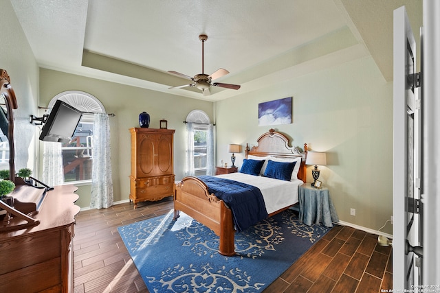 bedroom with dark wood-type flooring, a raised ceiling, and ceiling fan