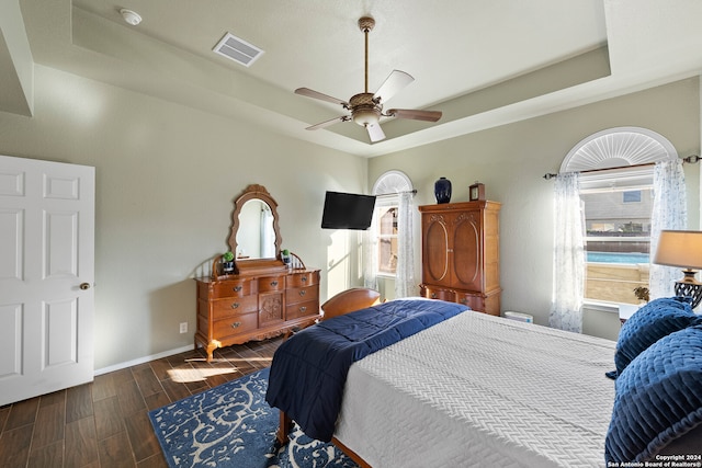 bedroom with dark wood-type flooring, ceiling fan, and a raised ceiling