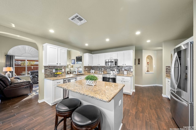 kitchen with dark wood-type flooring, stainless steel appliances, sink, a center island, and white cabinetry