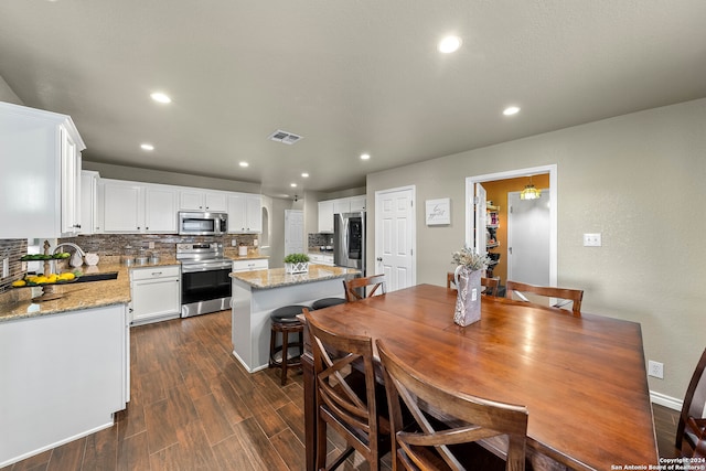 kitchen featuring light stone counters, dark hardwood / wood-style flooring, white cabinetry, stainless steel appliances, and a center island