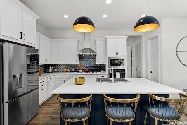 kitchen featuring stainless steel appliances, decorative light fixtures, sink, and wall chimney range hood