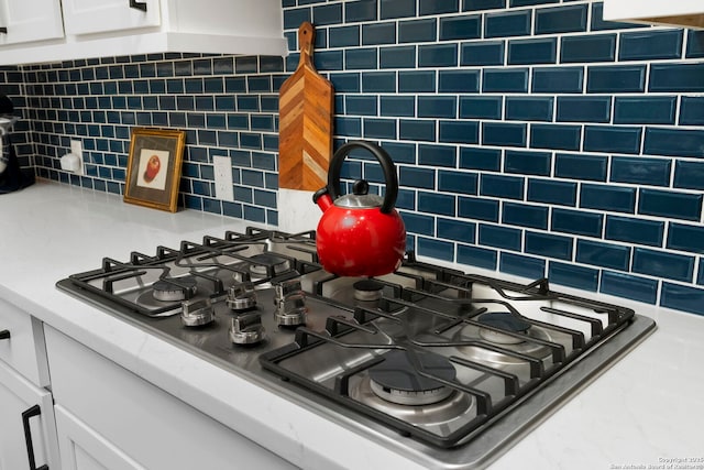 room details featuring stainless steel gas stovetop, white cabinets, and decorative backsplash