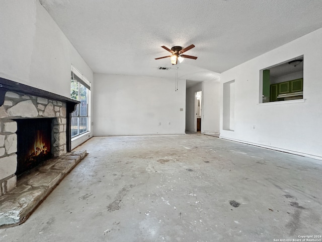 unfurnished living room featuring concrete flooring, a stone fireplace, a textured ceiling, and ceiling fan