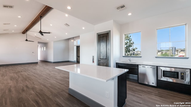 kitchen with vaulted ceiling with beams, dark wood-type flooring, stainless steel appliances, sink, and a center island