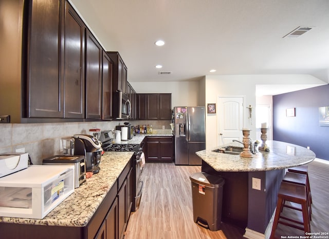 kitchen featuring appliances with stainless steel finishes, sink, a kitchen breakfast bar, light hardwood / wood-style flooring, and a center island with sink