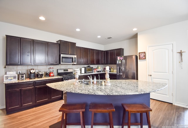 kitchen with a breakfast bar area, a kitchen island with sink, light hardwood / wood-style flooring, and stainless steel appliances