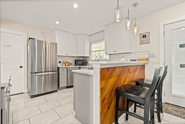 kitchen with a breakfast bar area, kitchen peninsula, white cabinets, decorative light fixtures, and appliances with stainless steel finishes