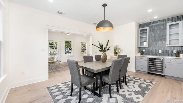 dining area featuring wine cooler, tile walls, bar area, and light hardwood / wood-style floors