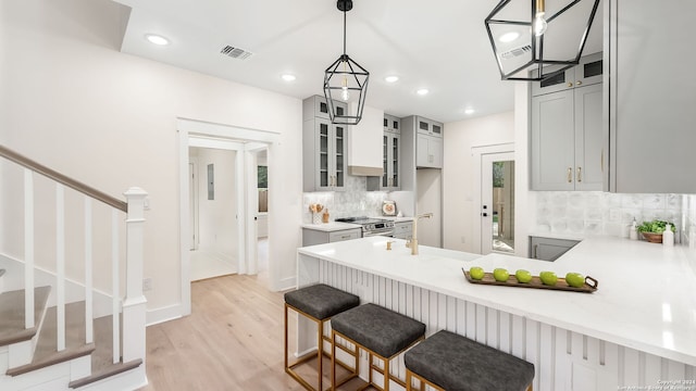 kitchen with tasteful backsplash, light wood-type flooring, kitchen peninsula, decorative light fixtures, and a breakfast bar