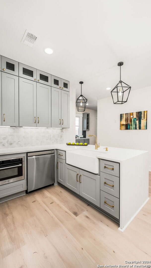 kitchen with appliances with stainless steel finishes, kitchen peninsula, decorative light fixtures, and light wood-type flooring