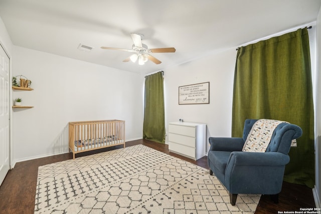 bedroom featuring ceiling fan, dark hardwood / wood-style floors, and a crib