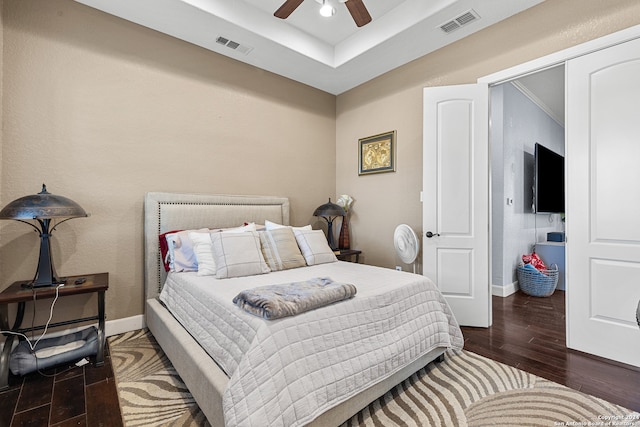 bedroom featuring a closet, a tray ceiling, dark wood-type flooring, and ceiling fan