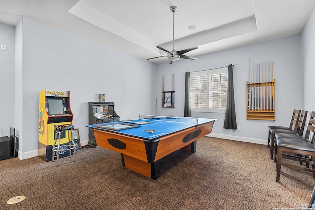 recreation room with a raised ceiling, dark carpet, and ceiling fan