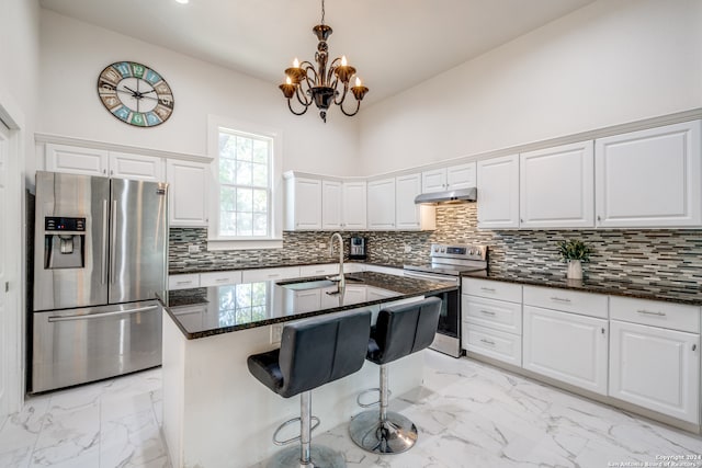 kitchen with a towering ceiling, sink, white cabinetry, stainless steel appliances, and a center island with sink