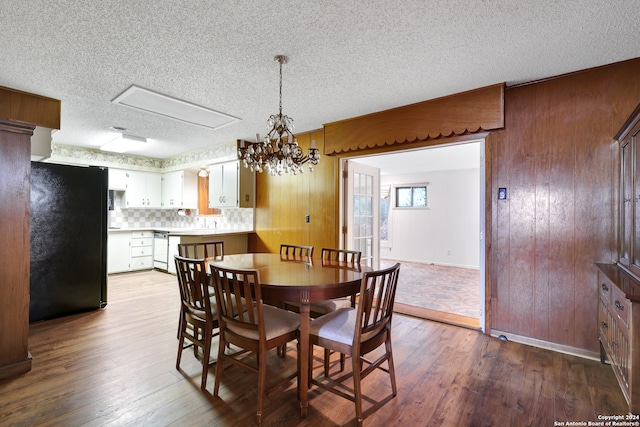 dining space featuring an inviting chandelier, a textured ceiling, hardwood / wood-style flooring, and wooden walls