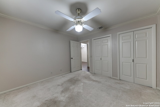 unfurnished bedroom with ornamental molding, two closets, light colored carpet, and ceiling fan