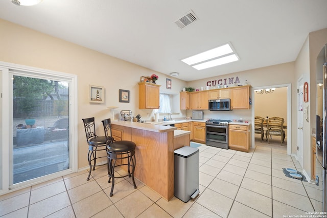 kitchen featuring a breakfast bar area, kitchen peninsula, light tile patterned floors, light brown cabinetry, and appliances with stainless steel finishes