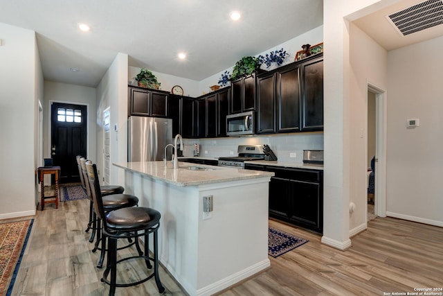 kitchen with light stone countertops, stainless steel appliances, sink, a center island with sink, and light hardwood / wood-style floors