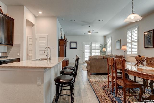 kitchen with light wood-type flooring, dark brown cabinetry, ceiling fan, sink, and pendant lighting