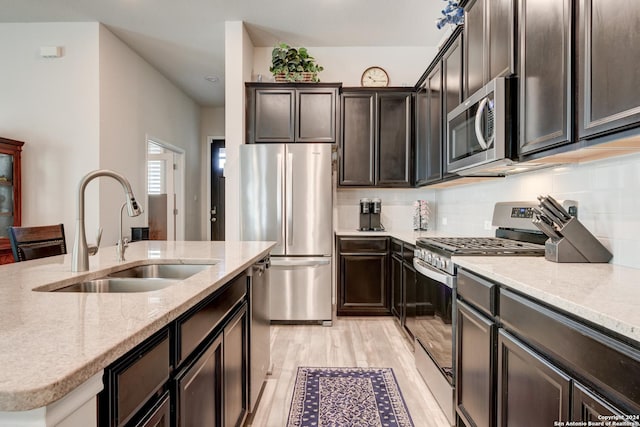 kitchen with backsplash, sink, light hardwood / wood-style flooring, appliances with stainless steel finishes, and light stone counters