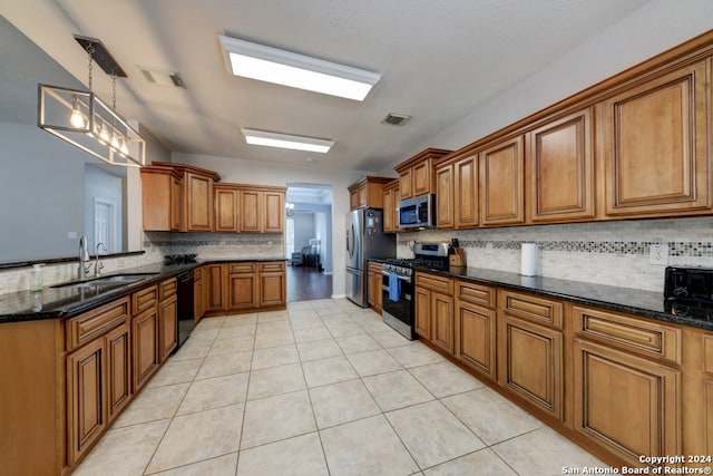 kitchen with decorative backsplash, appliances with stainless steel finishes, dark stone countertops, sink, and decorative light fixtures