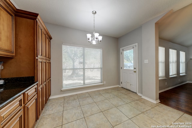 kitchen with light hardwood / wood-style flooring, an inviting chandelier, dark stone countertops, and decorative light fixtures