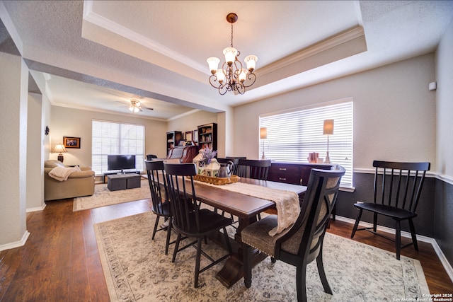 dining space with a tray ceiling, crown molding, dark hardwood / wood-style floors, and ceiling fan with notable chandelier