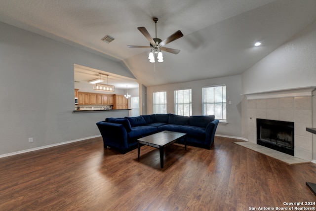 living room with ceiling fan with notable chandelier, a textured ceiling, dark hardwood / wood-style flooring, a tiled fireplace, and lofted ceiling