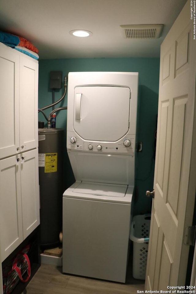 laundry area with cabinets, water heater, stacked washer and dryer, and light hardwood / wood-style floors