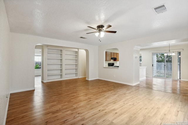 unfurnished living room featuring built in features, a textured ceiling, ceiling fan with notable chandelier, and light wood-type flooring