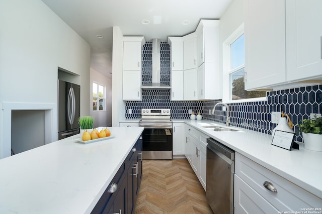 kitchen with white cabinetry, stainless steel appliances, wall chimney range hood, and light parquet flooring