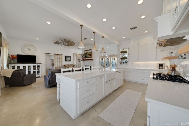 kitchen with decorative backsplash, white cabinets, a large island with sink, a barn door, and decorative light fixtures