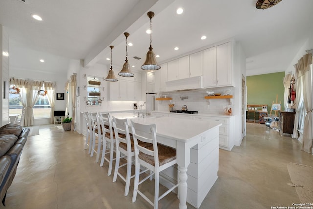 kitchen featuring tasteful backsplash, hanging light fixtures, a large island with sink, white cabinetry, and a kitchen bar