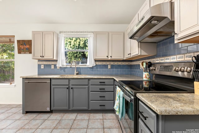 kitchen with appliances with stainless steel finishes, a healthy amount of sunlight, gray cabinetry, and range hood