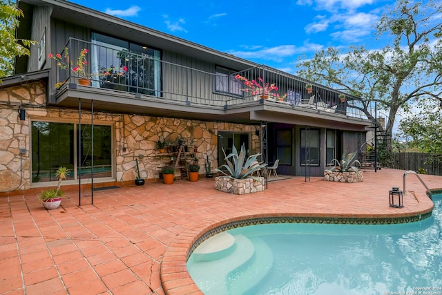 rear view of house with a fenced in pool, a patio area, and a balcony