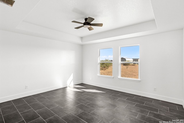 empty room with a textured ceiling, a tray ceiling, and ceiling fan