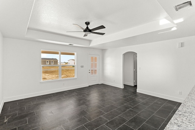 empty room with ceiling fan, a textured ceiling, and a tray ceiling