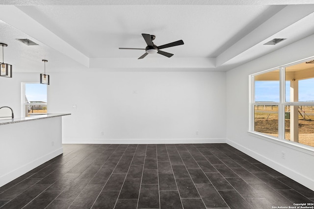 unfurnished living room with ceiling fan, a textured ceiling, a tray ceiling, and dark hardwood / wood-style flooring