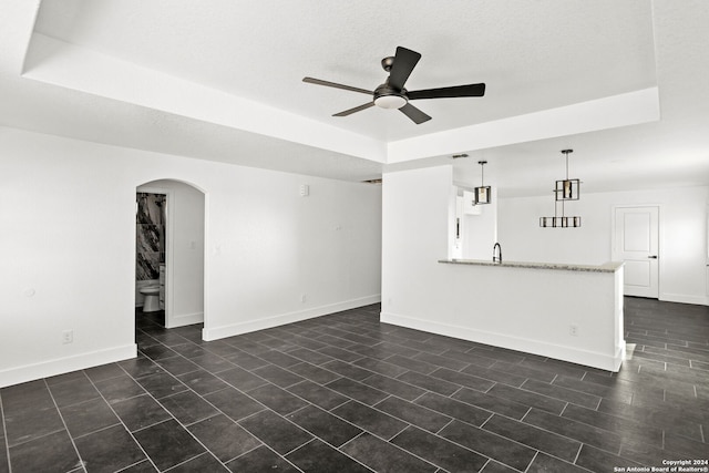 unfurnished living room featuring sink, a textured ceiling, a tray ceiling, and ceiling fan